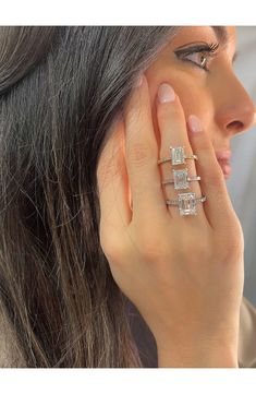 a woman holding her hand up to her ear with three diamond rings on top of it