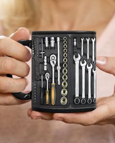 a woman holding a black coffee mug filled with wrenches and other tool tools in it