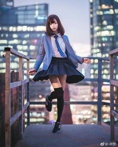 a woman in a skirt and jacket posing on a balcony with city lights behind her