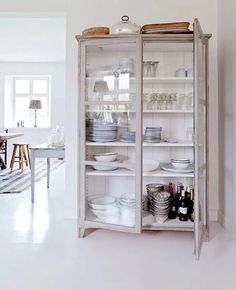 a white china cabinet filled with lots of dishes and wine bottles next to a dining room table