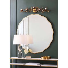 a mirror on the wall above a table with a lamp and vase in front of it