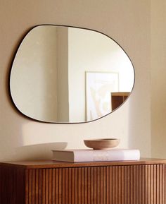 a round mirror on the wall above a wooden dresser with a bowl and book sitting on top