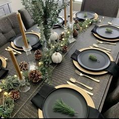 the table is set with black and gold place settings, pine cones, greenery, candlesticks, and silverware