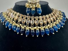 This exquisite navy blue Kundan Polki Choker Set with Jhumka and Tikka is a stunning piece of Indian jewelry that embodies elegance and tradition.Handcrafted with intricate detailing, this choker set features Kundan and Polki stones set in a gold-plated base, adding a touch of opulence to any outfit. The set includes matching Jhumka earrings and a Tikka, completing the look with grace and charm. Designed with a blend of Indian and Pakistani influences, this jewelry set is perfect for special occ Blue Cutdana Necklace Bollywood Style, Blue Chandbali Kundan Necklace Bollywood Style, Traditional Blue Kundan Necklace With Tilla, Blue Kundan Necklace Bollywood Style For Festivals, Blue Kundan Necklace With Cutdana For Wedding, Festive Blue Kundan Necklace With Cutdana, Blue Chandbali Kundan Necklace For Festive Occasions, Blue Kundan Necklace With Tilla For Diwali, Blue Bollywood Kundan Necklace For Festivals