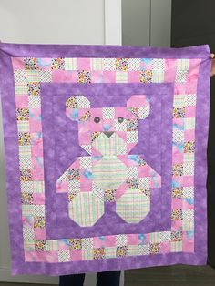 a person holding up a purple quilt with a teddy bear on it's back