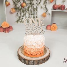 an orange and white cake sitting on top of a tree stump next to peaches