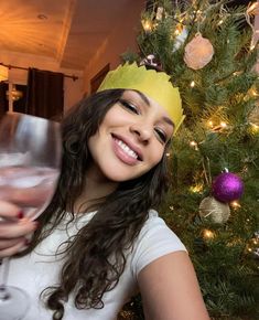 a woman wearing a paper crown holding a wine glass in front of a christmas tree