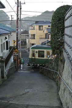 a green and white train traveling down tracks next to houses on the side of a hill