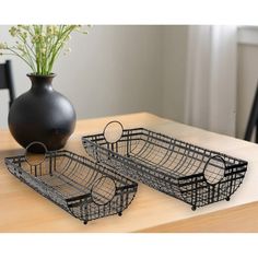 two metal trays sitting on top of a wooden table next to a black vase