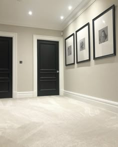 an empty room with three black doors and pictures on the wall above it, along with carpeted flooring