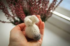 a hand holding a tiny stuffed animal next to some flowers