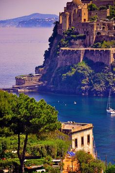 an old castle sits on top of a hill overlooking the ocean and boats in the water