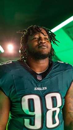 a football player with dreadlocks standing in front of a green background wearing a jersey