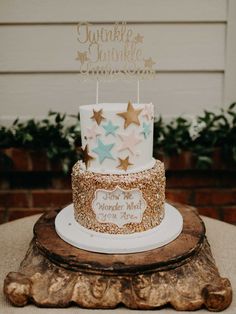 a three tiered cake with gold stars on top and a name sign that says twinkle twinkle