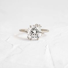 an engagement ring with a round diamond in the center on a white background, close up