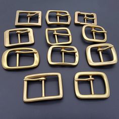 six pairs of square buckles on a black surface, each with a gold finish