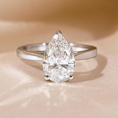 a pear shaped diamond ring sitting on top of a table