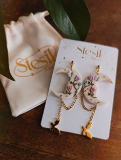 a pair of earrings sitting on top of a wooden table next to a white bag