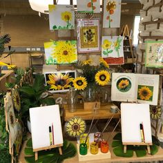 an assortment of sunflowers are displayed on a table with easels and paintings