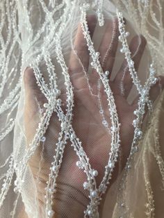 a hand is holding some white beaded beads on a sheer net material fabric that has been sequined onto it