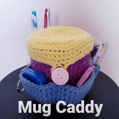 there is a crocheted hat with buttons on it and the words mug caddy next to it