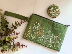 a green pouch with flowers on it next to a plant and a small embroidered coin purse