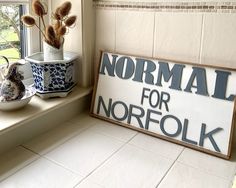 a sign that says normal for norfolk next to a potted plant on a window sill