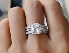 a woman's hand with two wedding rings on top of her finger and the ring has an oval shaped diamond surrounded by smaller round diamonds