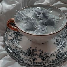 a cup filled with water and silver leaves on top of a saucer, next to a plate