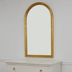 a white dresser with a gold framed mirror on top