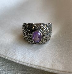 Stunning art deco style silver ring with encrusted in marcasite with an oval amethyst coloured glass stone. This one is hard to date - it looks to possible have a hallmark/stamp but it is hard to make out. It has a beautiful deco style and could be from the 20s-40s.  This would be a lovely engagement ring or celebratory gift...to yourself or someone else! Condition: Great condition with some scratching as to be expected from wear  Label: 925 Content: silver, marcasite, amethyst coloured stone Size on Label: n/a Measurements: Size 6 *IMPORTANT NOTE: All measurements are taken with the garment lying flat and then doubled. Please leave some wiggle room for comfort. *SALES ARE FINAL: Please make any inquiries prior to purchase. All clothing is pre-owned unless specified and comes with a certai