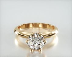 a yellow gold engagement ring with a round cut diamond in the center, on a white background