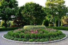 a circular garden area with flowers and trees in the back ground, surrounded by brick pavers