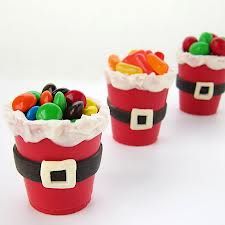 three red cups with candy in them on a white surface, decorated like santa claus