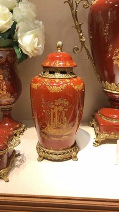 three red vases with gold designs on them are sitting on a table next to white flowers