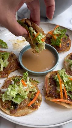 a person dipping something into a bowl of sauce on top of some bread with lettuce and carrots