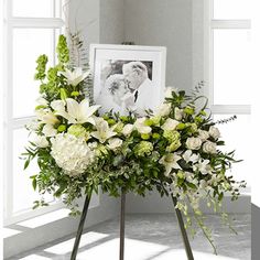 a bouquet of white flowers on a stand in front of a window with a framed photo