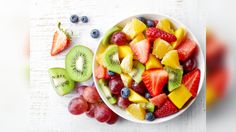 a white bowl filled with fruit next to sliced kiwis and strawberries on top of a table