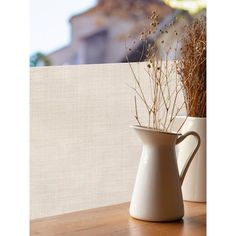 two vases with dried plants in them sitting on a wooden table next to a window