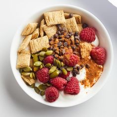 a bowl filled with cereal, nuts and raspberries on top of a white table