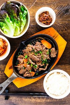 an iron skillet filled with meat and vegetables on top of a wooden cutting board