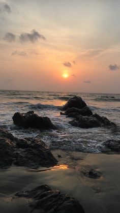 the sun is setting over the ocean with rocks in the foreground