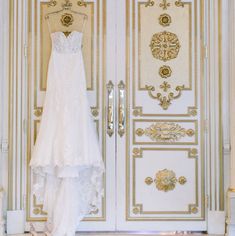 a wedding dress hanging on a door in front of a gold and white wall with ornate designs