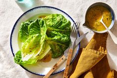 a plate with lettuce and mustard on it next to a spoon, knife and fork