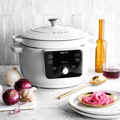 a white crock pot sitting on top of a counter next to onions and garlic