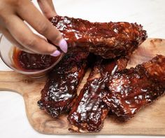 someone is dipping sauce into ribs on a cutting board