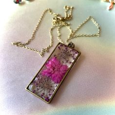 This One Of A Kind Pendant Features Purple Dried Flowers Cast In Resin In An Antique Bronze Plated Rectangle Frame, Hung On An 18” Chain. Handmade Purple Rectangular Necklace, Gold Resin Flower Pendant Necklace, Multicolor Resin Pendant Jewelry, Serotonin Necklace, Handmade Purple Resin Necklace, Elegant Resin Flower Pendant Jewelry, Purple Flower Shaped Necklace With Pressed Flowers, Silver Dragonfly Necklace, Ceramic Beads Necklace