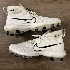 a pair of white nike cleats sitting on top of a wooden floor