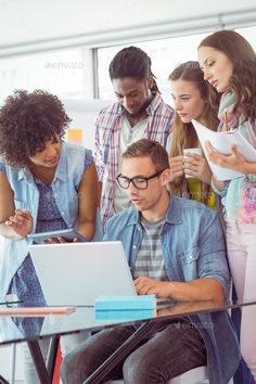 a group of young people gathered around a laptop in an office - stock photo - images