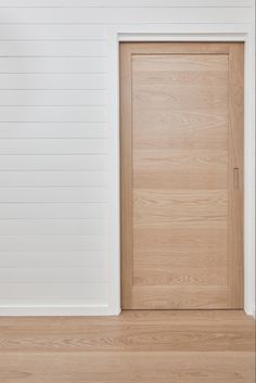 an empty room with a wooden door and hard wood flooring in front of a white wall